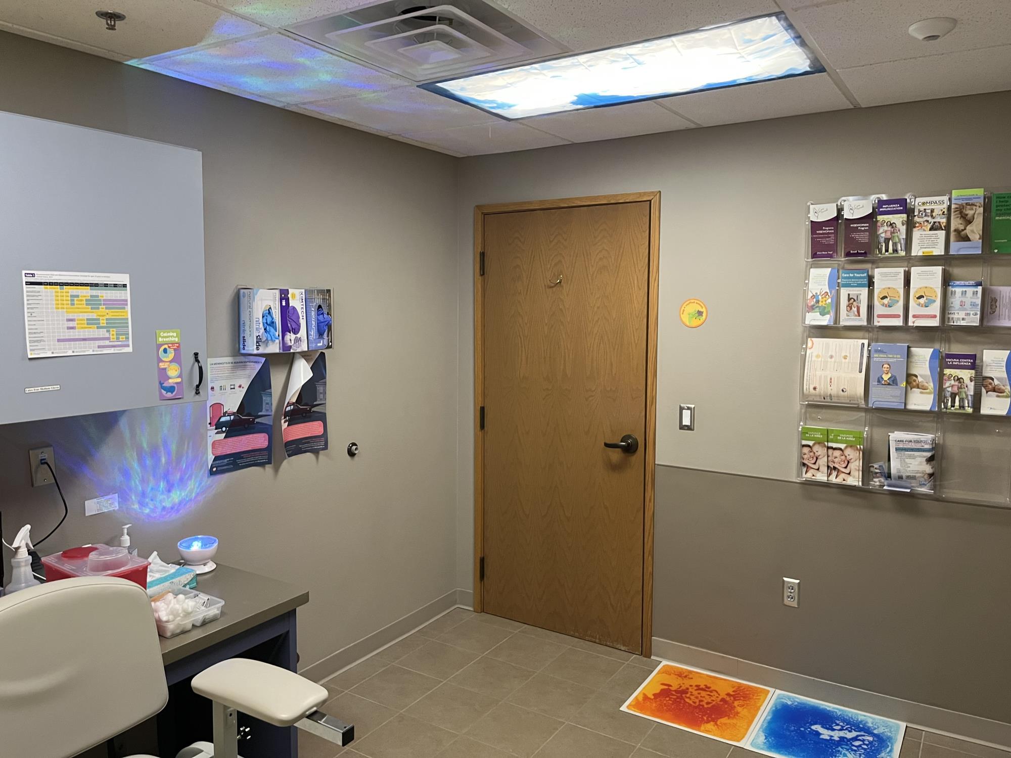 exam room with light covers, colored tiles on the floor, light and sound machine on counter, brochures on wall, chair in corner