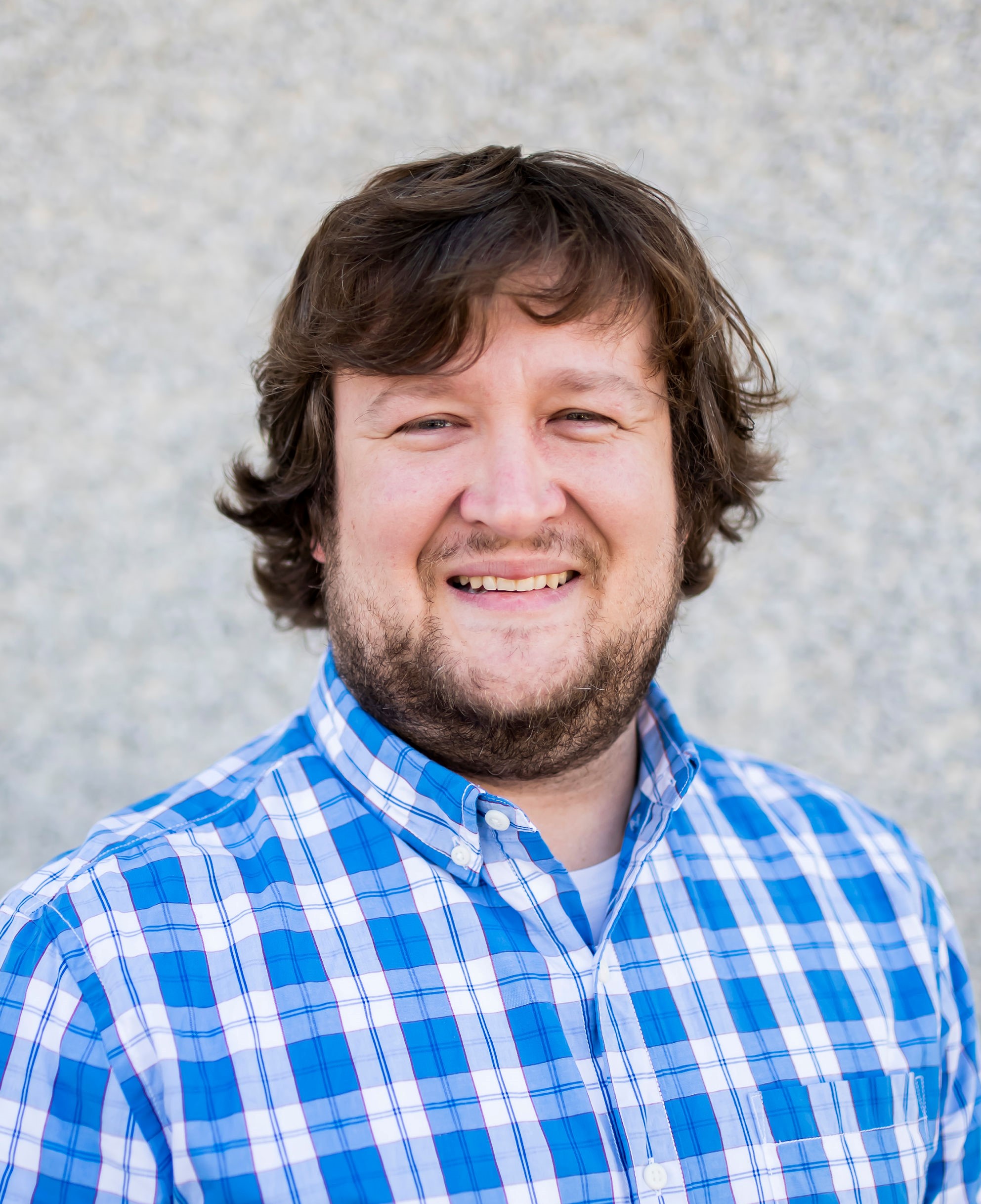 Man with short dark hair, beard and mustache, blue and white pattern shirt smiling