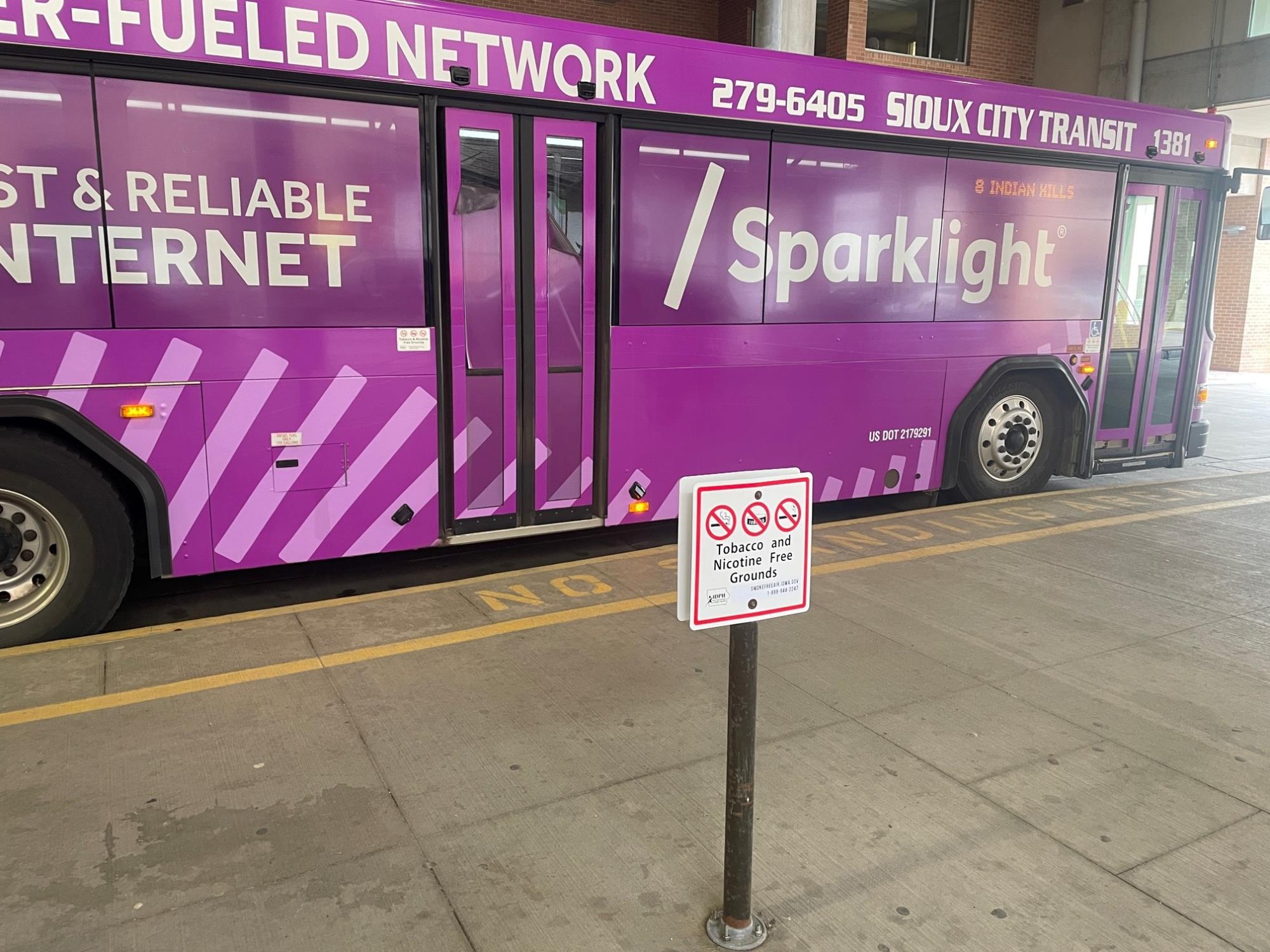 Tobacco and Nicotine Free Sign posted in ground with a purple wrapped city bus in the background