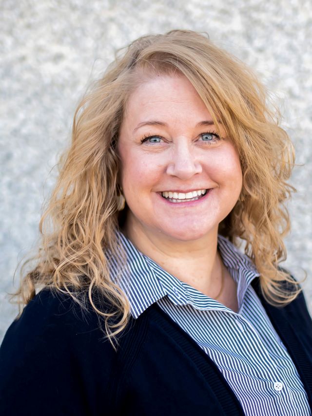 woman with curly shoulder length hair with blue and white stripped shirt and sweater on smiling