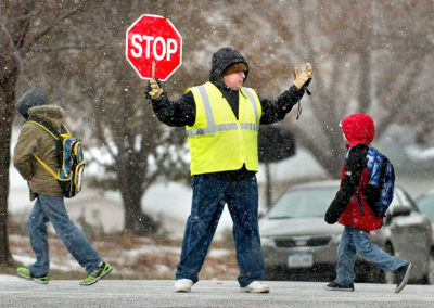 Crossing Guard holding a stop sign while kids cross the street while snowing. treet Spalding Park