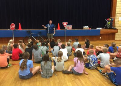 students sitting on a gym floor with adult stands in front of them