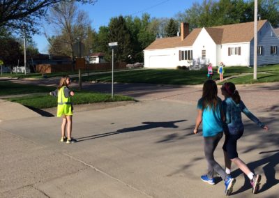 Student safety patrol with yellow vest standing in crosswalk while kids cross the street