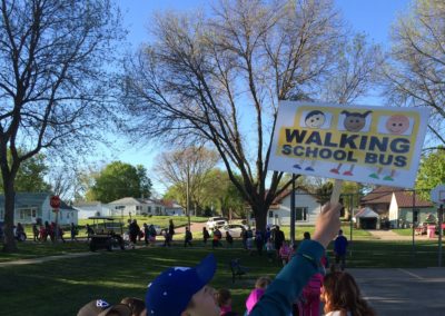 Student holding up walking school bus sign in the back of a long line of kids walking to school