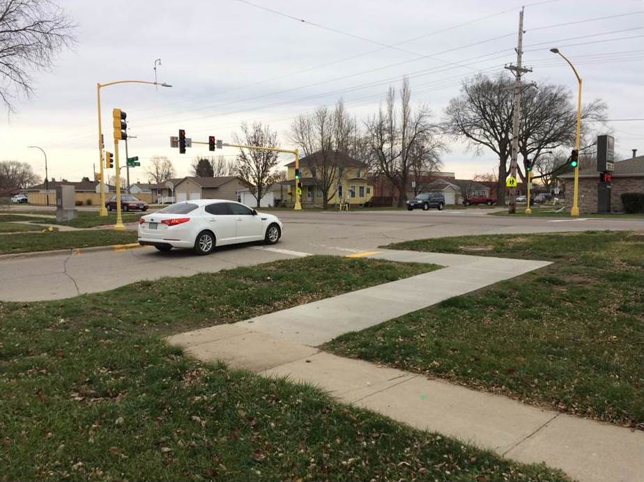 Sidewalk and curb cut that goes in front of a stopped car at a stop light.