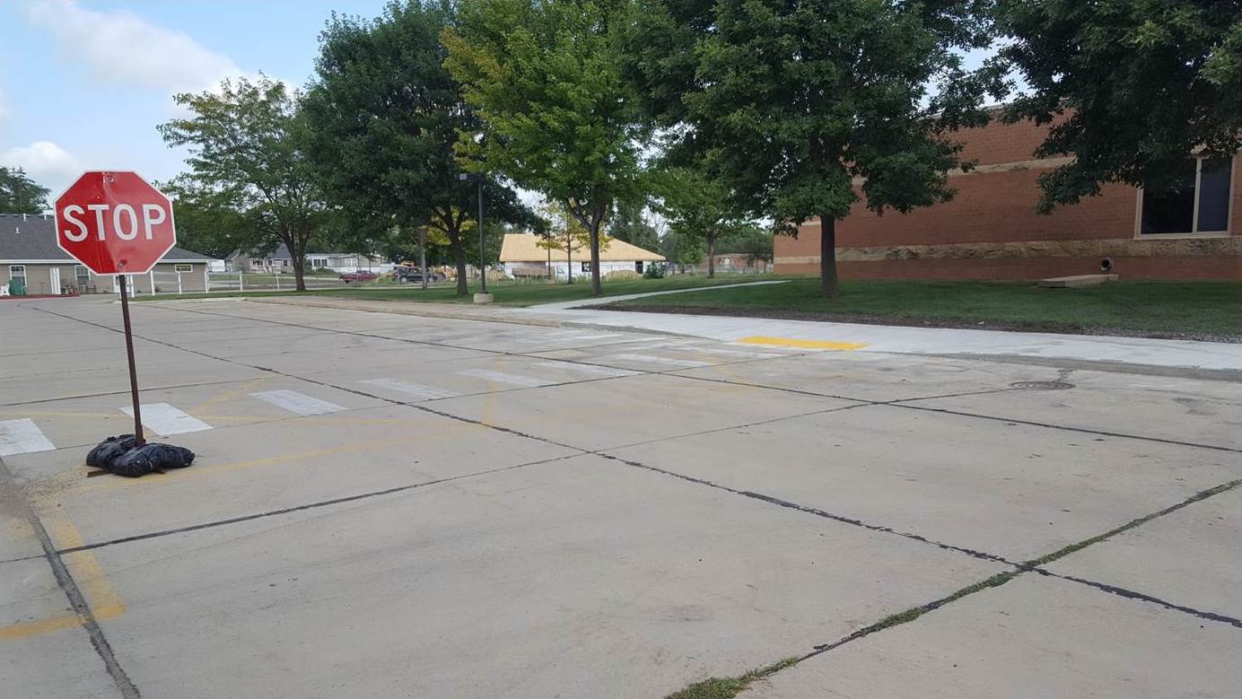 Crosswalk and movable stop sign placed in front of crosswalk. Crosswalk connects to a curb cut and sidewalk by a school